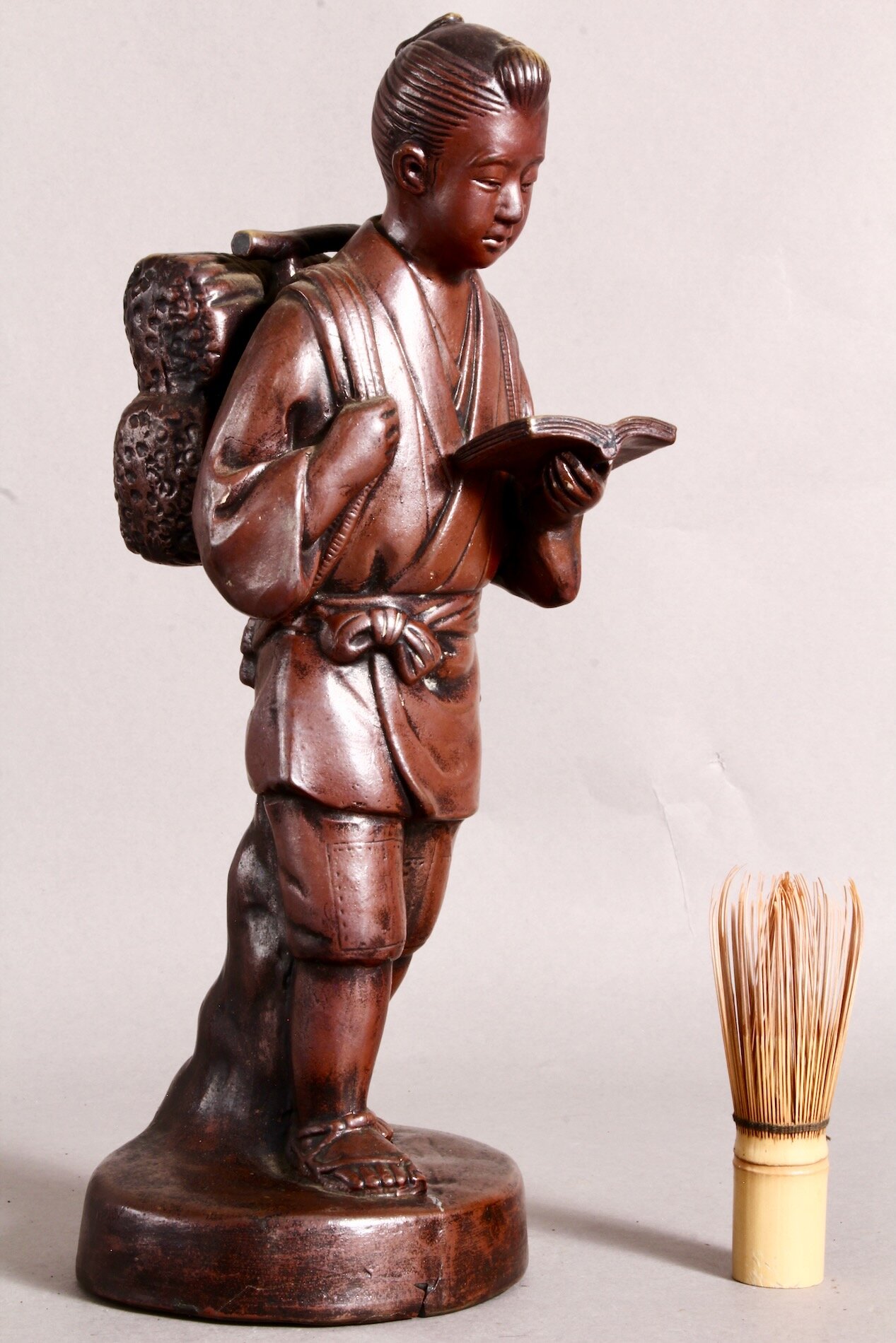 Ninomiya Kinjirou – japanische Bronzefigur mit Buch und Feuerholz, daneben ein Matcha-Besen als Größenreferenz