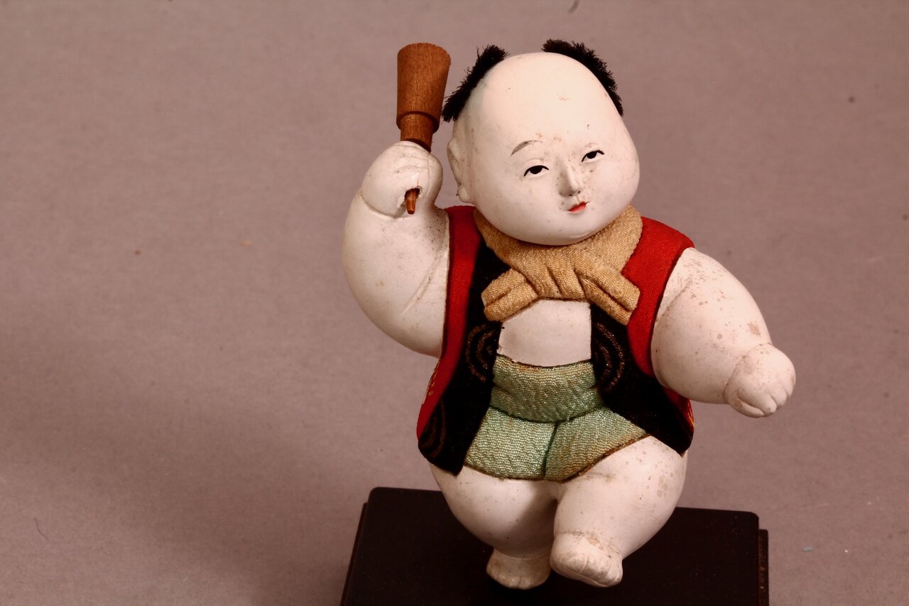Stofffigur in traditioneller Darstellung mit Keule auf Sockel