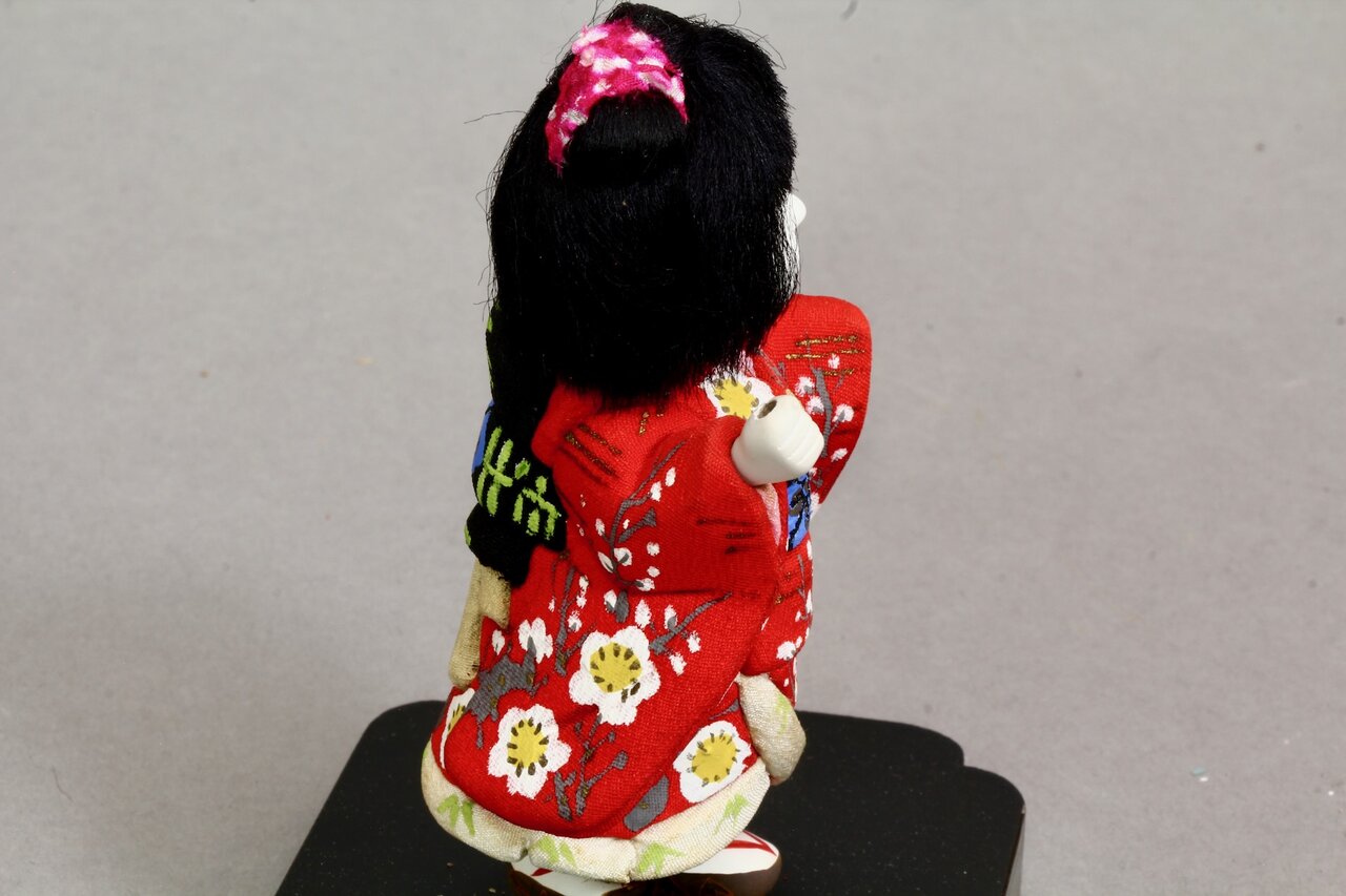 Stoffpuppe mit schwarzem Haar und rotem Kimono von hinten