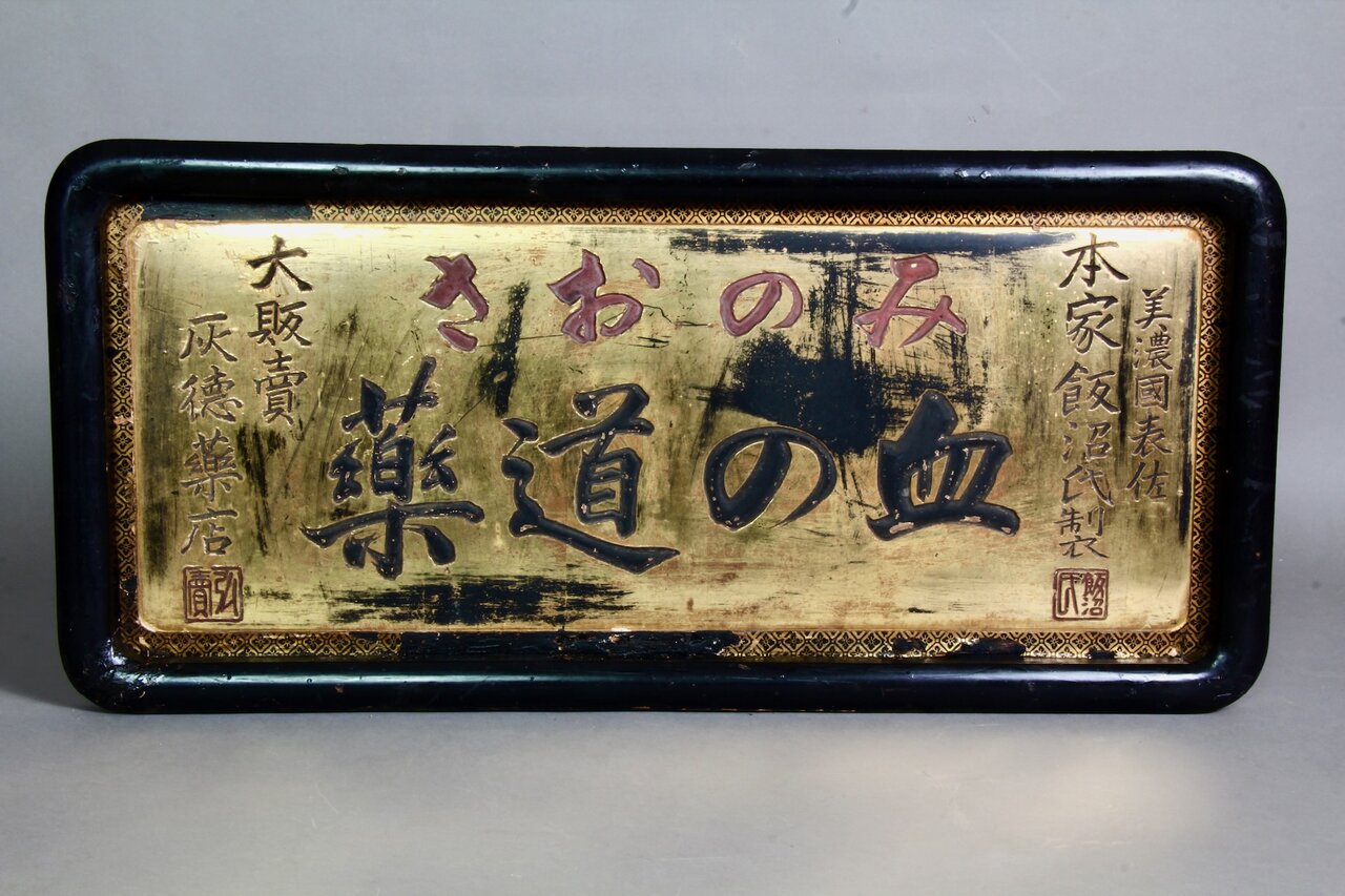 Lackiertes Firmenschild mit schwarzen und roten Schriftzeichen auf goldenem Hintergrund